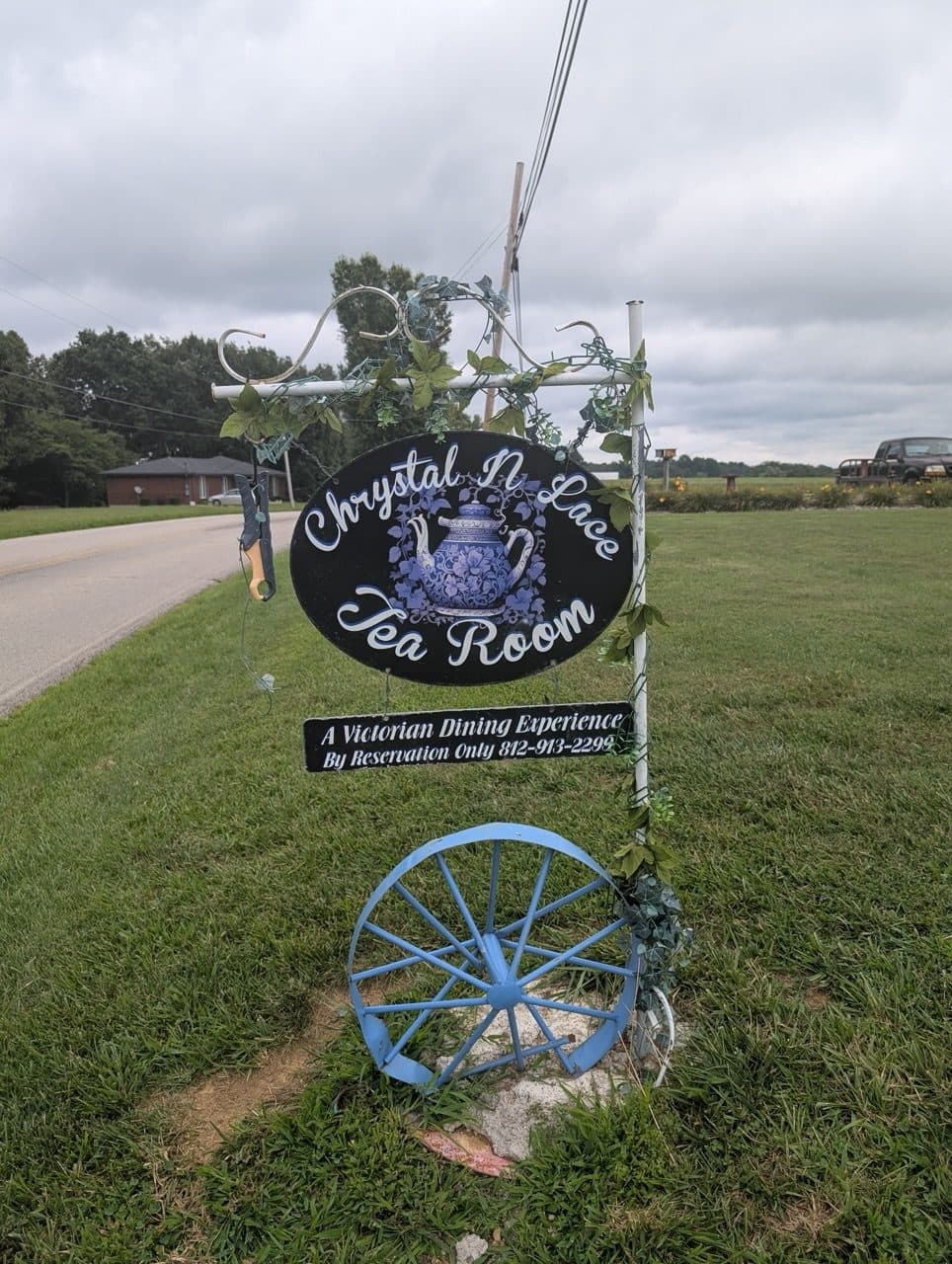 The oval Chrystal N Lace Tea Room sign at the roadside above a blue wagon wheel
